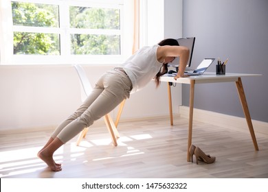 Side View Of A Young Businesswoman Doing Push Up On Office Desk - Powered by Shutterstock