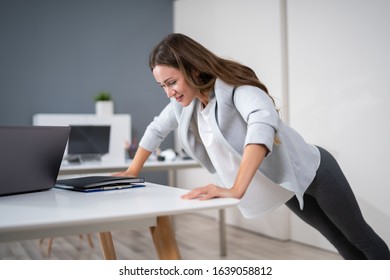 Side View Of A Young Businesswoman Doing Push Up On Office Desk - Powered by Shutterstock