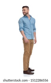 Side View Of A Young Casual Man With Blue Shirt Standing And Looking Back Over Shoulder Happy On White Studio Background