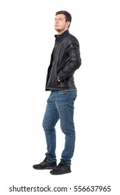 Side View Of Young Casual Man With Hands In Leather Jacket Pockets Looking Up Serious. Full Body Length Portrait Isolated Over White Background.