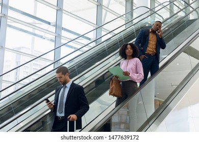 Side view of a young Caucasian businessman using smartphone, a young African American businesswoman holding a file and a young African American businessman on the phone coiming down an escalator in a - Powered by Shutterstock