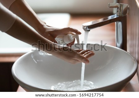 Side view young cautious woman applying antibacterial soap on hands, doing regular sanitizing routine in bathroom at home, preventing spreading covid 19 corona virus infection, healthcare concept.