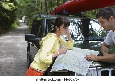 Side View Of A Young Couple Looking At Map On Car Bonnet In The Forest