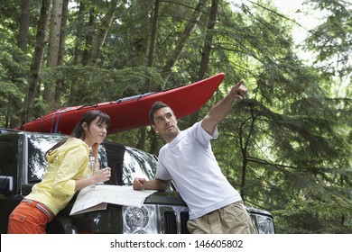 Side View Of A Young Couple With Map On Car Bonnet In The Forest