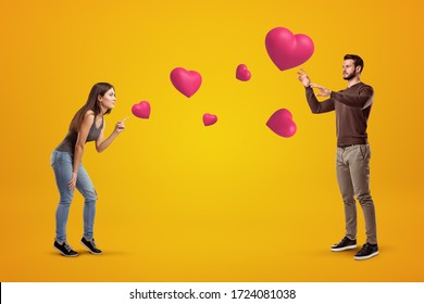 Side view of young couple on amber background playing with cute valentine hearts that float in air, man trying to catch one heart. St. Valentine's. Love and affection. - Shutterstock ID 1724081038