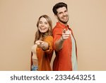 Side view young couple two friends family man woman wear casual clothes point index finger camera you stand back to back together isolated on pastel plain light beige color background studio portrait