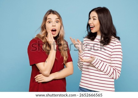 Side view young couple two friends women wearing red casual clothes together gossip and tells secret sharing news isolated on pastel plain light blue cyan background studio portrait. Lifestyle concept