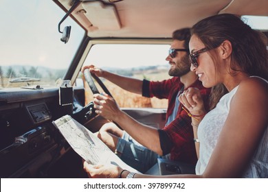 Side View Of Young Couple Using A Map On A Roadtrip For Directions. Young Man And Woman Reading A Map While Sitting In A Car.