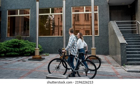 Side View Of Young Couple Walking With Bicycles On City Street. Modern Urban Healthy Lifestyle. Entertainment, Leisure And Hobby. Biking. Man And Smiling Caucasian Girl Enjoying Time Together