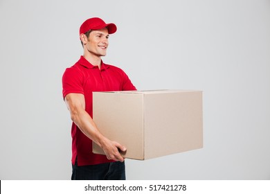 Side View Of Young Delivery Man With Box. Isolated Gray Background