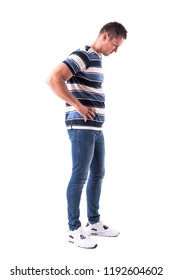 Side view of young disappointed sad man looking down with hands on hips. Full body isolated on white background.