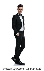 Side View Of Young Elegant Man In Tuxedo Smiling And Walking Isolated On White Background, Full Body