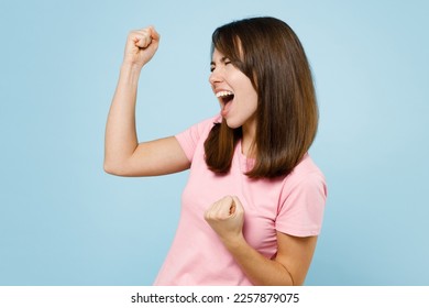 Side view young excited happy caucasian woman 20s in pink t-shirt doing winner gesture celebrate clenching fists say yes isolated on pastel plain light blue background studio. People lifestyle concept - Shutterstock ID 2257879075