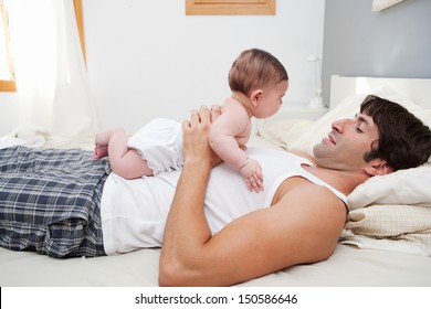 Side View Of A Young Father Holding His New Born Baby Daughter On His Chest While Laying Down On A Bed At Home, Enjoying Quality Time Together.