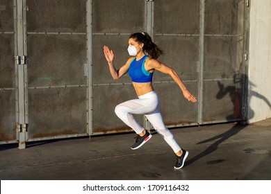 Side View Of Young Female Athlete Running Fast Outside Wearing Face Mask In The City. Sporty Woman Training With Protection Against Coronavirus.