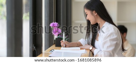 Side view of young female college student take short note while reading text to prepare for her final exam 