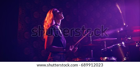 Side view of young female drummer performing in illuminated nightclub