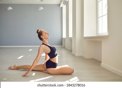 Side View Of Young Female Gymnast In Crop Top And Shorts Doing Stretching Exercise In New Studio. Beautiful Barefoot Woman In Sportswear Sitting In Graceful Pose On Gym Floor