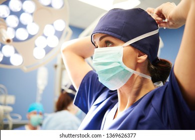 Side View Of Young Female Surgeon Tying Her Surgical Mask 