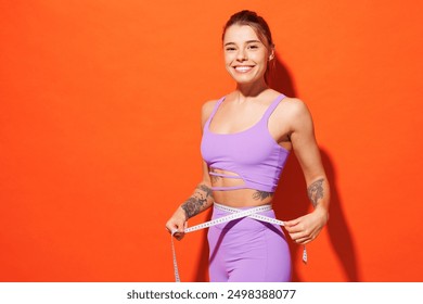 Side view young fitness trainer sporty woman sportsman wearing purple top clothes spend time in home gym hold measure tape on waist isolated on plain orange background. Workout sport fit abs concept - Powered by Shutterstock