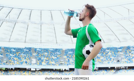 side view of young football player in green t-shirt holding ball while drinking water - Powered by Shutterstock