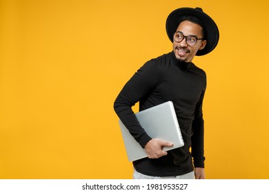 Side view of young freelancer smiling copywriter african man 20s wear stylish black shirt hat eyeglasses walk with closed laptop pc computer look aside isolated on yellow background studio portrait. - Powered by Shutterstock