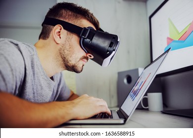 Side view of young freelancer using vr technology while working on analysis for monthly salary on stock market. On displays are charts. Home office interior.
