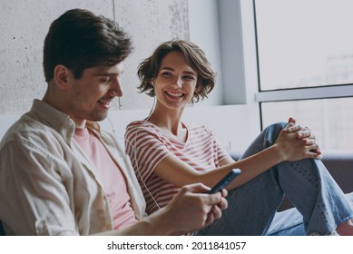 Side View Young Fun Couple Two Friends Woman Man In Casual Clothes Earphones Sitting On Sofa Use Mobile Cell Phone Listen Music New Playlist Rest Indoors At Home Flat Together People Lifestyle Concept