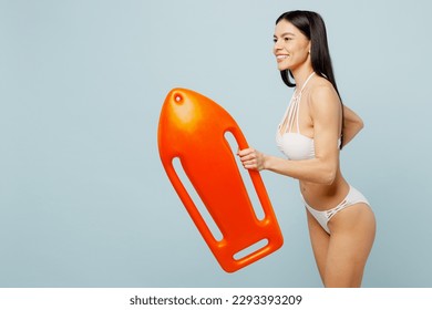 Side view young fun lifeguard woman wear swimsuit near hotel pool hold in hand lifebuoy run fast hurry up isolated on plain pastel light blue cyan background. Summer vacation sea rest sun tan concept