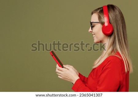 Side view young fun woman she wears red shirt casual clothes glasses raise up hands dance listen to music in headphones look aside isolated on plain pastel green background studio. Lifestyle concept