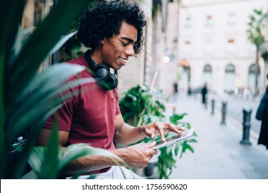Side view of young guy with black hair in casual clothes using gadgets and sitting on bench on street in city - Powered by Shutterstock