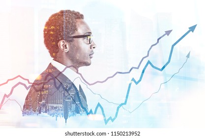 Side View Of A Young Handsome African American Businessman Wearing Glasses And A Gray Suit. Growing Graphs Against A Foggy City Background. Toned Image Double Exposure