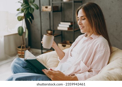 Side view young happy calm woman wear casual clothes sits in armchair read book drink coffee tea stay at home hotel flat rest relax spend free spare time in living room indoor Lifestyle lounge concept - Powered by Shutterstock