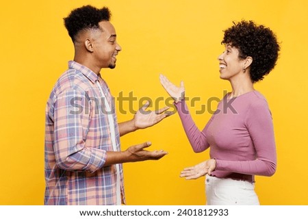 Side view young happy couple two friend family man woman of African American ethnicity wear purple casual clothes together talk speak look to each other meet isolated on plain yellow orange background