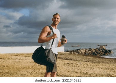 Side view young happy strong athletic toned fit sportsman man wear sports clothes bag drink protein shake warm up train at sunrise sun dawn over sea beach outdoor on pier seaside in summer day morning