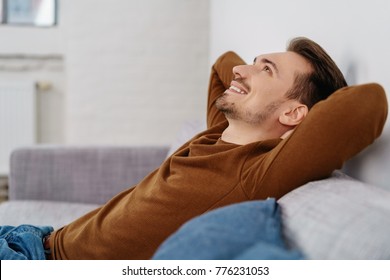 Side view of young hapy relaxed man sitting on sofa at home