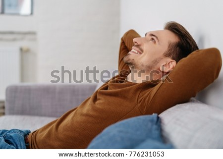 Side view of young hapy relaxed man sitting on sofa at home