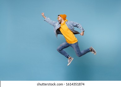 Side view of young hipster guy in fashion jeans denim clothes posing isolated on pastel blue background. People lifestyle concept. Mock up copy space. Jumping with outstretched hand like Superman