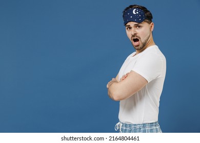 Side view young indignant sad man 20s wearing pajamas jam sleep mask white t-shirt resting relaxing at home hold hands crossed folded isolated on dark blue background. Bad mood night bedtime concept
