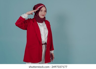 Side view of young Indonesian woman in a red jacket and hijab is doing salute gesture, isolated by blue background. Indonesia Independence Day concept. - Powered by Shutterstock