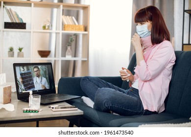 Side View Of Young Lady Sitting On Sofa At Home In Protective Mask And Using Laptop Pc While Talking With Confident Experienced Male Doctor Online, Telling Results Of CT Scan.