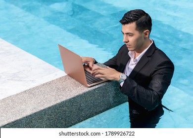 Side view. Young male businessman in a business suit works for a laptop while standing in the water in the pool. Remote work. Freelancer - Powered by Shutterstock