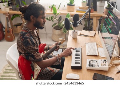 Side view of young male musician adjusting sound of electronic synthesizer and looking at computer screen in home studio - Powered by Shutterstock