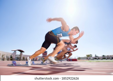 Side view of young male sprinters leaving their starting blocks at the start of a sprint race on a bright, sunny day at the track - Powered by Shutterstock