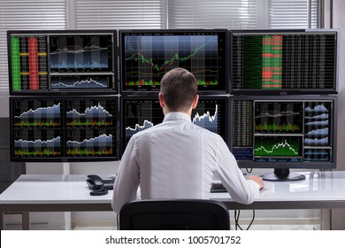 Side View Of A Young Male Stock Market Broker Analyzing Graphs On Multiple Computer Screens