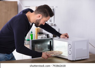 Side View Of A Young Man Baking Pizza In Microwave Oven