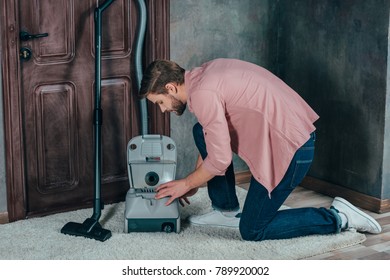 Side View Of Young Man Fixing Broken Vacuum Cleaner At Home