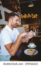 Side view of young man having cup of coffee and pastry while texting in a cafe