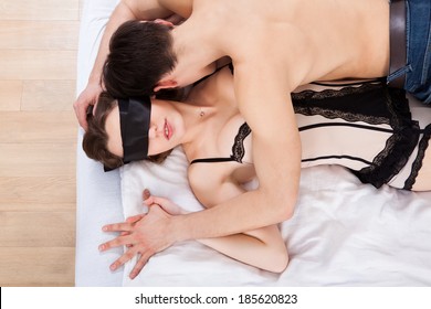 Side View Of Young Man Kissing Sexy Blindfolded Woman In Bed At Home Side View Of Young Man Kissing Sexy Blindfolded Woman In Bed At Home