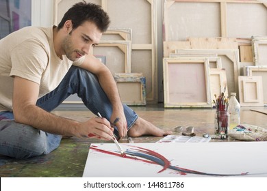 Side view of a young man painting on canvas on studio floor